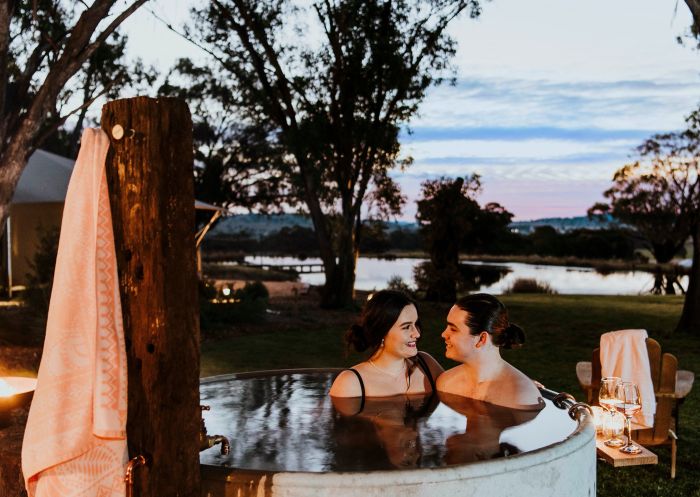 Couple relaxing in hot tub with sun setting behind them at Evamor Valley, Mudgee