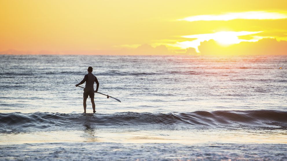 Man heading out for a morning of stand-up paddleboarding at Tathra Beach, Tathra