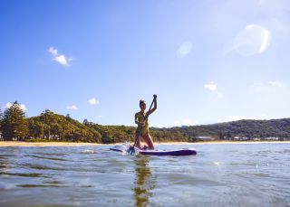Woman enjoying a morning of stand up paddleboarding at Pearl Beach on the Central Coast