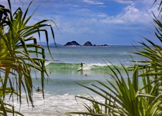 Surfers catching waves off Watgos Beach in Byron Bay with views across to Julian Rocks