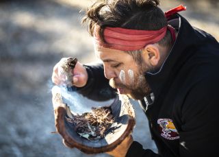 Aboriginal guide Dwayne Bannon-Harrison performing a smoking ceremony during a traditional welcome on a Ngaran Ngaran Culture Awareness tour, South Coast