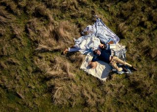 航拍照片显示，一对情侣躺在埃文斯平原威尔加车站的草地上，身上盖着毯子。