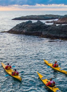 Three kayakers on the water near some rocks looking out to the ocean, Guerilla Bay - Credit: Eurobodalla Coast Tourism