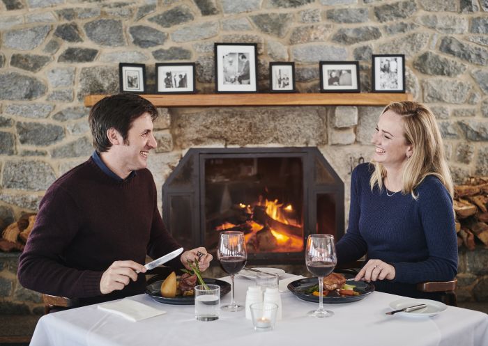 A couple enjoying a meal by the fireplace at Marritz Hotel in Perisher