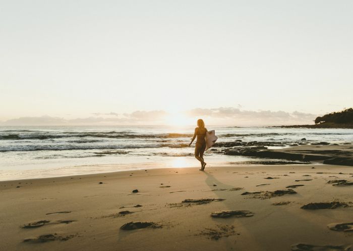 Woman heading out for a morning surf at Angourie Point Beach, Angourie