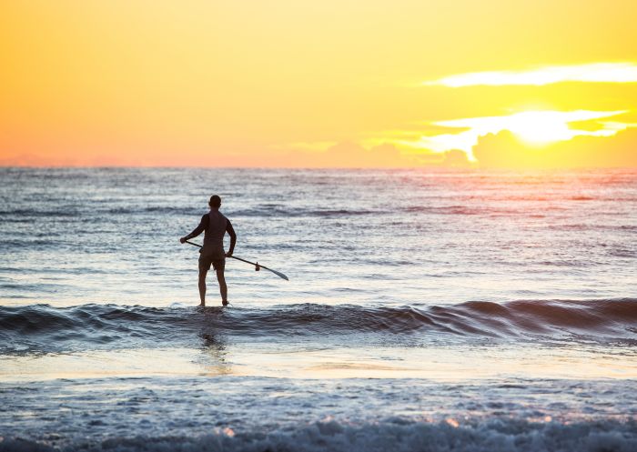 Ein Mann macht sich auf den Weg zum Stand-Up-Paddling am Tathra Beach in Tathra, Saphirküste. 