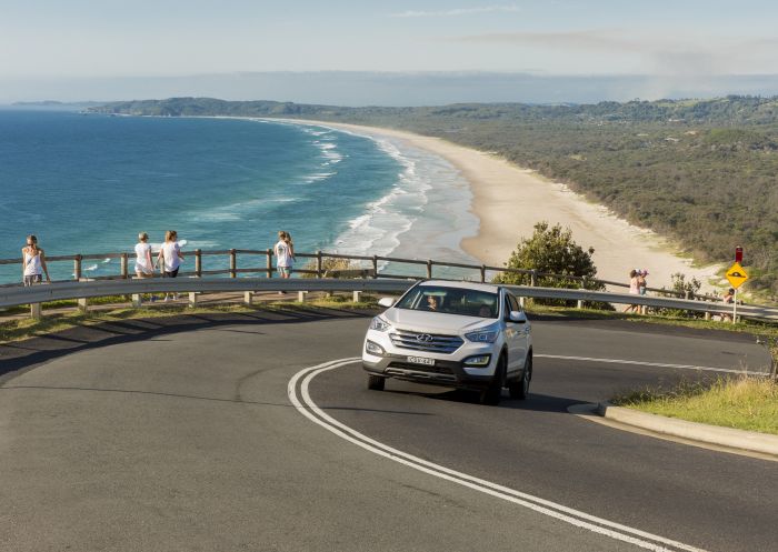 Car driving along the coast with Tallow Beach, Byron Bay in the background