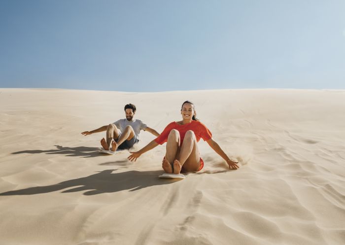 Couple enjoying a sandboarding experience at Stockton Bight Sand Dunes located in the Worimi Conservation Lands