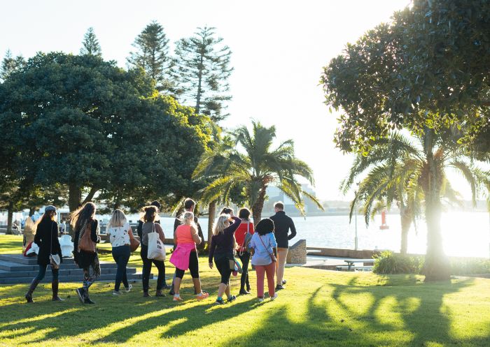 A small group walks on Newcastle foreshore on a guided Newcastle Afoot walking tour