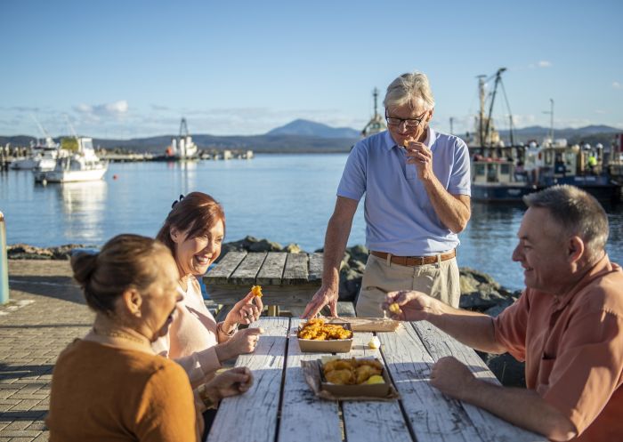 Couples enjoying fish and chips by the water at Twofold Bay in Eden, Sapphire Coast