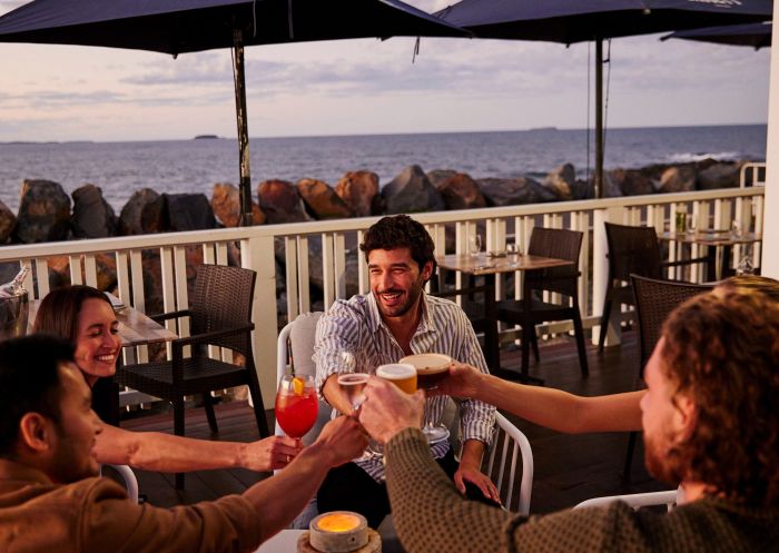 Freunde genießen Drinks auf dem Balkon des Restaurants Latitude 30 in Coffs Harbour. 