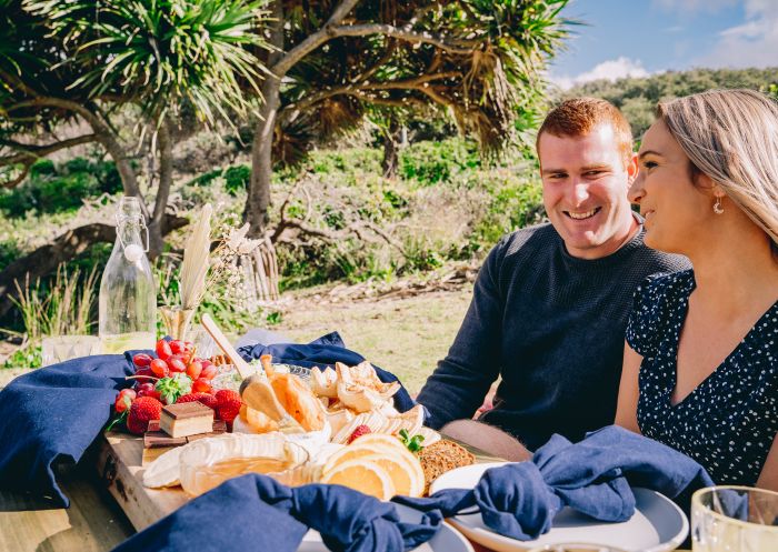 Couple enjoying a romantic picnic set up by Fuller Food Co at Little Bay Picnic Area - South West Rocks
