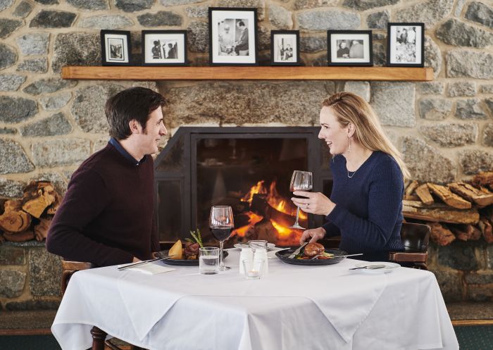 Couple enjoying a meal by the fireplace at Marritz Hotel, Perisher