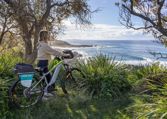 Woman with e-bike overlooking beach, Narooma