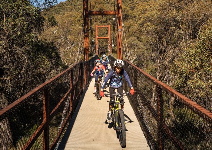 A family bike rides across a suspension bridge along Thredbo Valley Track, Kosciuszko National Park
