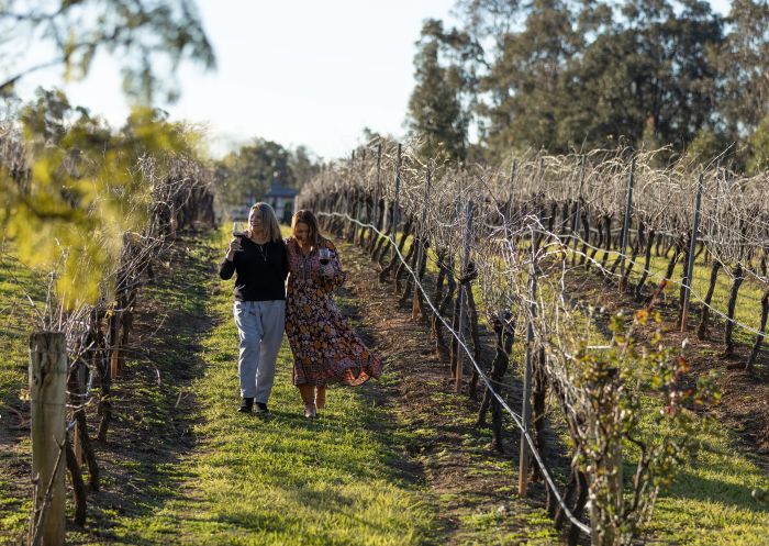 Women strolling through the vineyards holding wine glasses at Tintilla Estate, Pokolbin