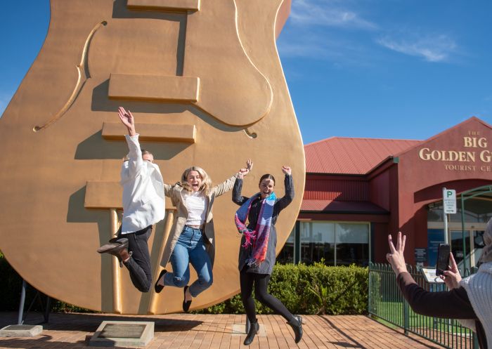 Friends jumping in front of the Golden Guitar attraction at The Big Golden Guitar Tourist Centre, Tamworth
