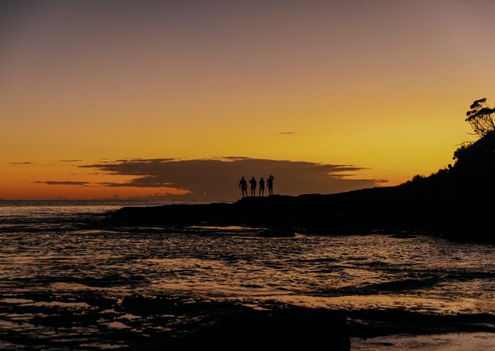 Friends standing together, watching the sunrise from a rock at NRMA Murramarang Beachfront Holiday Resort, South Durras