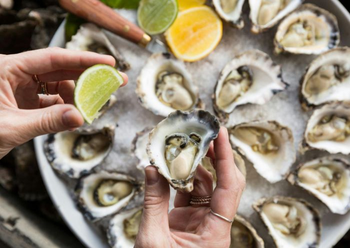 A plate of shucked rock oysters, a ladies hand is holding a lemon, about to squeeze and feast, Narooma Oyster Festival, Narooma - Credit: Eurobodalla Shire Council