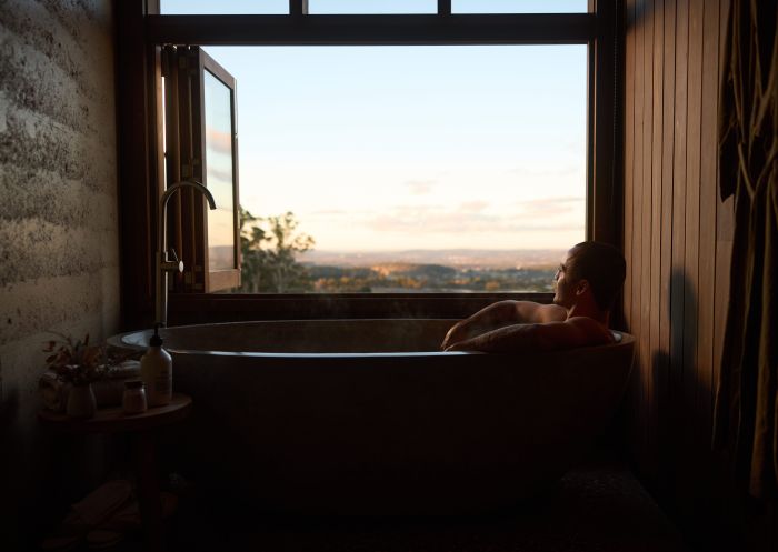 Man enjoys a relaxing bath looking out to the country scenery at Basalt Luxury Accomodation, Canobolas