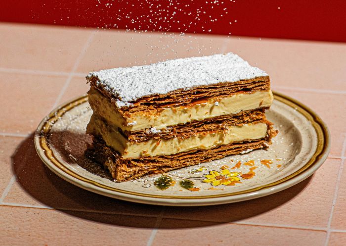 Picture of a layered vanilla slice on a plate with icing sugar being dusted on top, Peaches Patisserie, Dorrigo - Credit: Lou Walpole