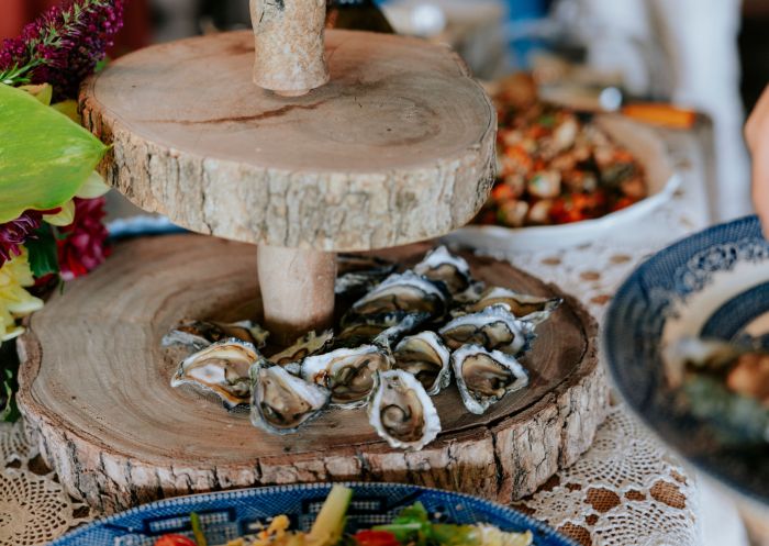 A tiered serving tray of oysters and some plates of starters on a VIP Private Tours, Old Mill Road Farm, Narooma