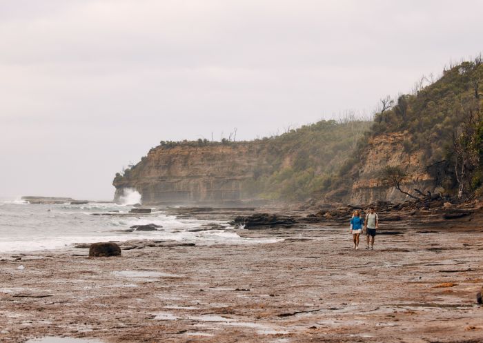  Couple walking with cliff in background, Pebbly Beach , Murramarang National Park