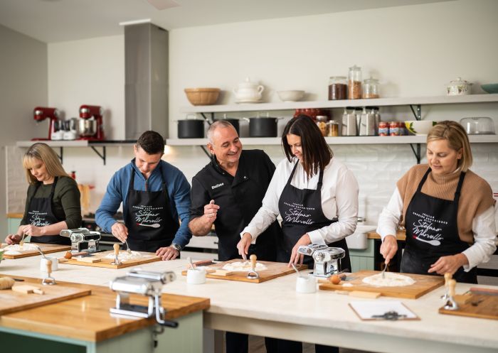 People in a cooking class kitchen while chef looks on with a smile, Bowral