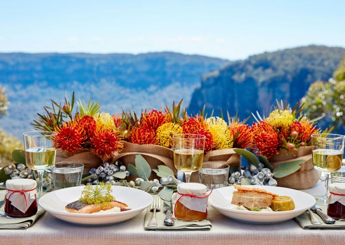 A gourmet food spread in front of colourful native flowers looking out to a mountain scene at The Lookout Echo Point, Katoomba - Credit: Trippas White Group
