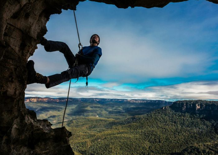 Man abseiling in the foreground with spectacular mountain views behind him, Wentworth Falls - Credit: David Hill | Blue Mountains Lithgow and Oberon Tourism