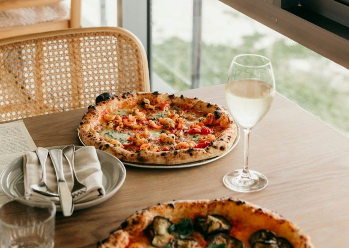 Two pizzas and wine glasses on timber table, Capiche Restaurant, East Ballina - Credit: Capiche