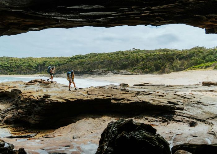 Two people walking over rocks with Emily Miller Beach in the background - Credit: Department of Planning and Environment (NSW)