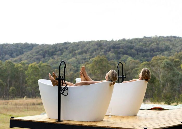 A couple enjoying twin outdoor baths on a deck looking out to tree covered hills in Rylstone - Credit: Into The Wild Escapes