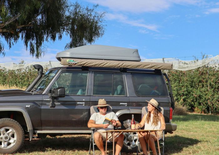 Couple enjoying a drink next to their SUV at The Apple Orchard campsite, Canobolas - Credit: Hipcamp Australia Pty Ltd
