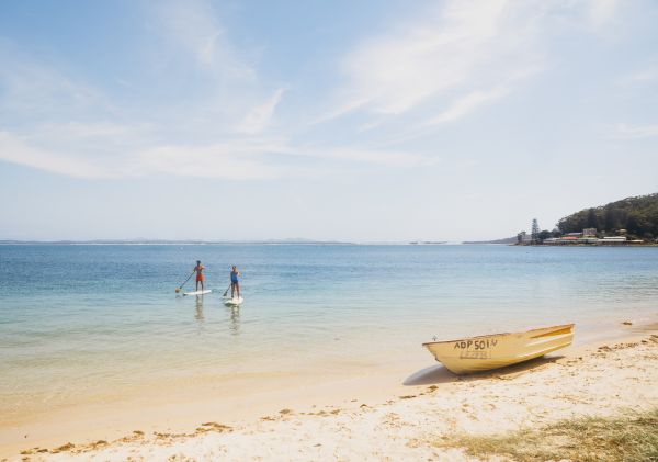 Couple enjoying a stand up paddleboarding experience in Shoal Bay, Port Stephens