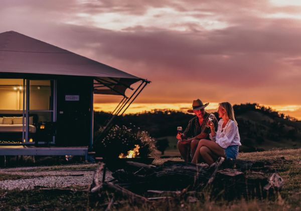 一对情侣在日落时分于马奇的塞拉伊斯凯普豪华露营地（Sierra Escape Luxury Glamping）的篝火旁享用一杯葡萄酒——图片来源：塞拉伊斯凯普