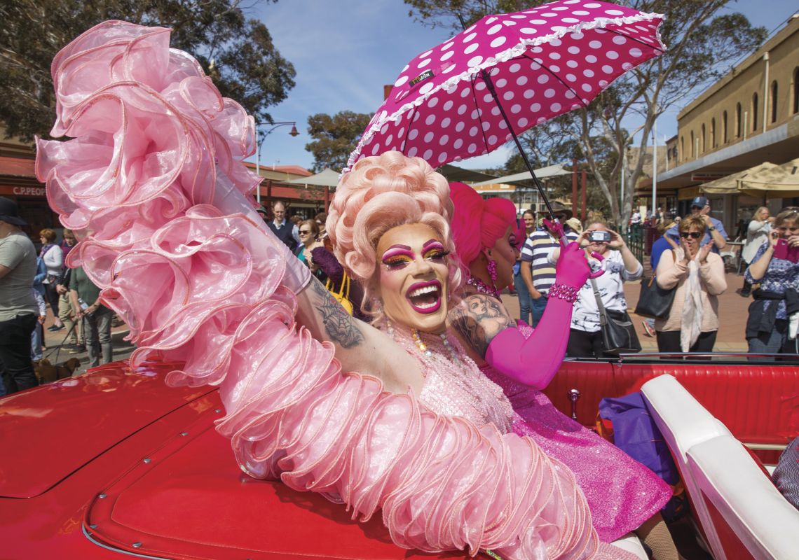 Brightly dressed drag queens ride through Broken Hill in a convertible during the Broken Heel Festival
