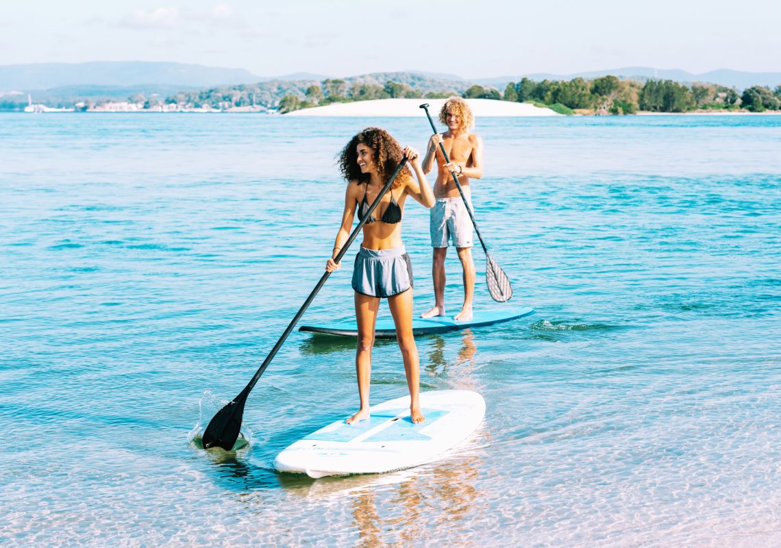 Friends enjoying stand up paddle boarding at Naru Beach in Lake Macquarie, North Coast