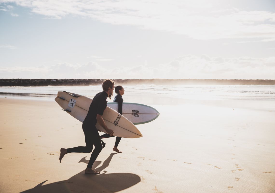 Surfer, die sich zum morgendlichen Surfen an den Turners Beach in Yamba, Clarence Valley, begeben.