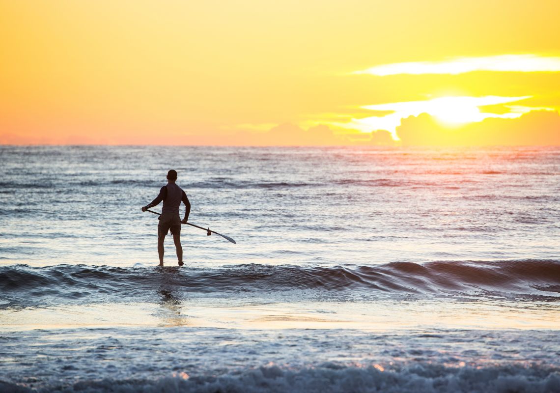 Man heading out for a morning of stand-up paddleboarding at Tathra Beach in Tathra, Sapphire Coast 