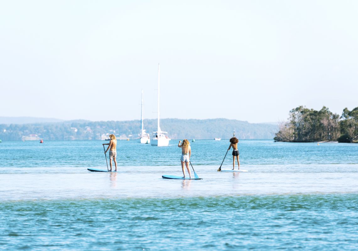 Friends enjoying a day of stand up paddleboarding on Lake Macquarie off Naru Beach
