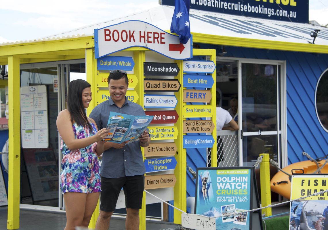Couple looking at an activity brochure outside the Bay Booking Office in Nelson Bay