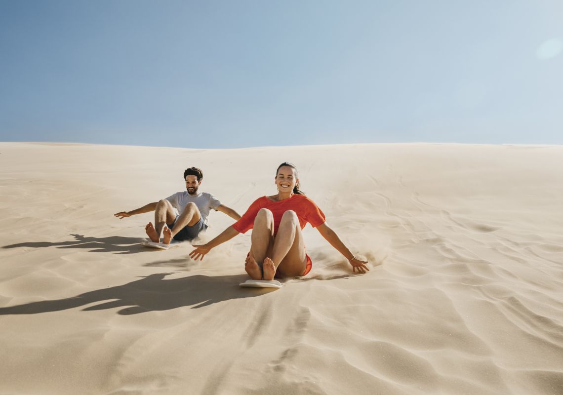 Couple enjoying a sandboarding experience at Stockton Sand Dunes located in the Worimi Conservation Lands