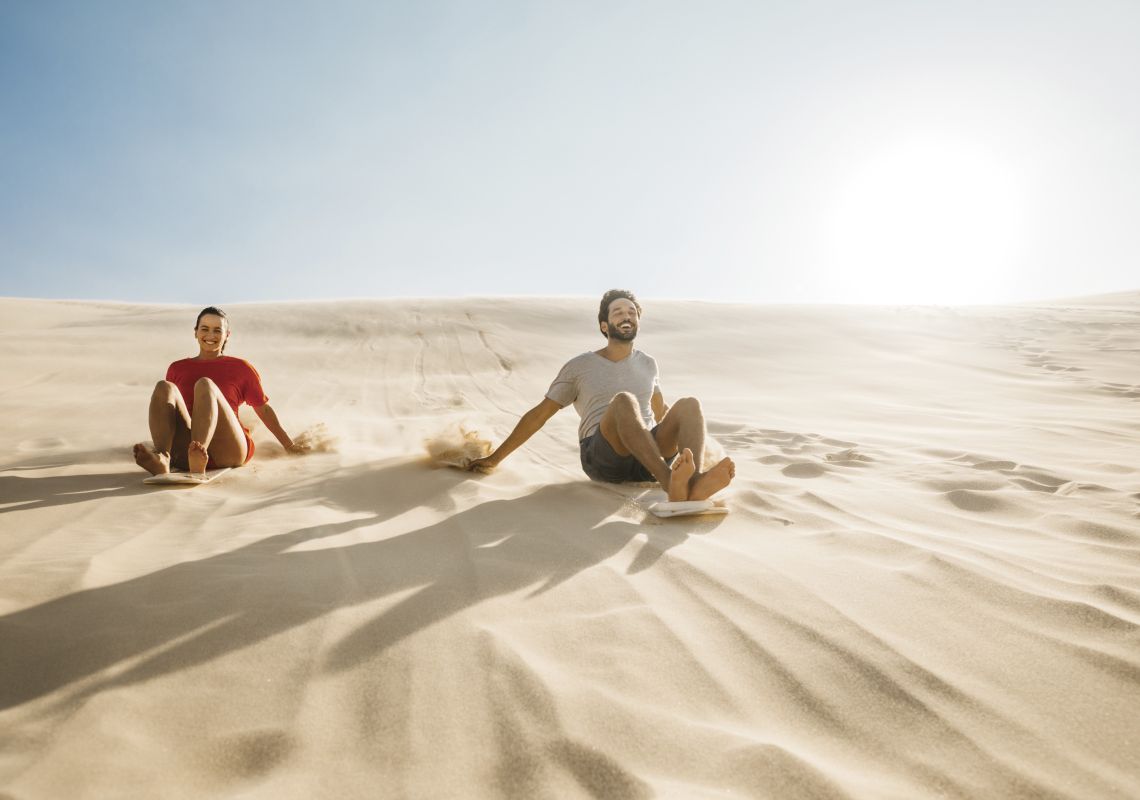 Couple enjoying a sandboarding experience at Stockton Sand Dunes located in the Worimi Conservation Lands