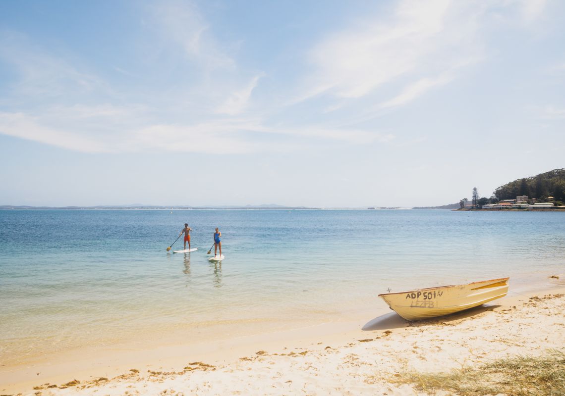 Couple enjoying a stand up paddleboarding experience in Shoal Bay, Port Stephens