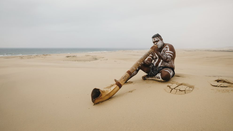 Aboriginal man playing the didgeridoo (didjeridu) on the Stockton Sand Dunes, Port Stephens, North Coast