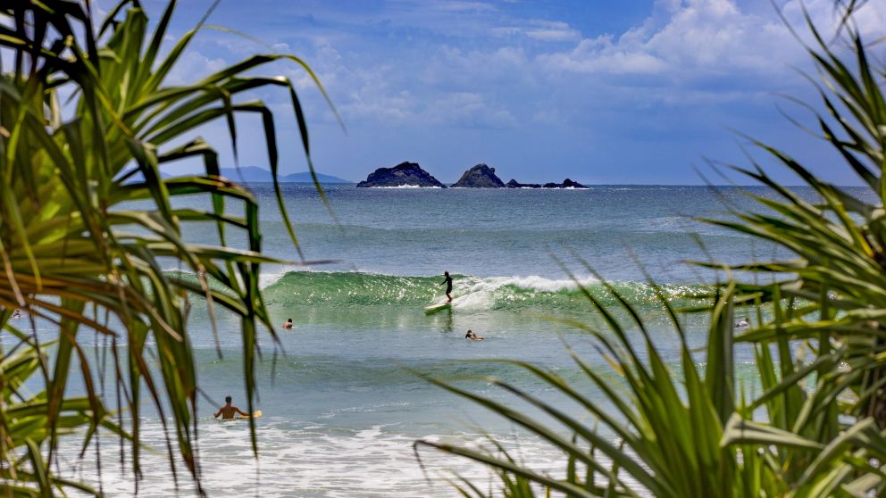 Surfers catching waves off Watgos Beach in Byron Bay with views across to Julian Rocks