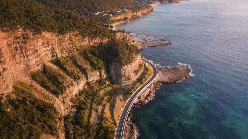 Aerial overlooking cars driving along Sea Cliff Bridge, Clifton