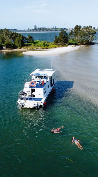  Aerial over waters with two people floating near houseboat, Forster Houseboat Hire, Forster