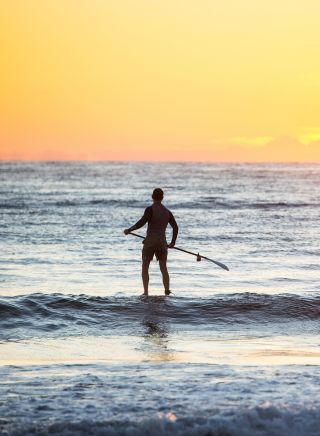 Man heading out for a morning of stand-up paddleboarding at Tathra Beach in Tathra, Sapphire Coast 